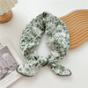 Écharpe en coton à motif floral vert et blanc nouée en nœud, posée sur une surface claire à côté d'un objet en bois.