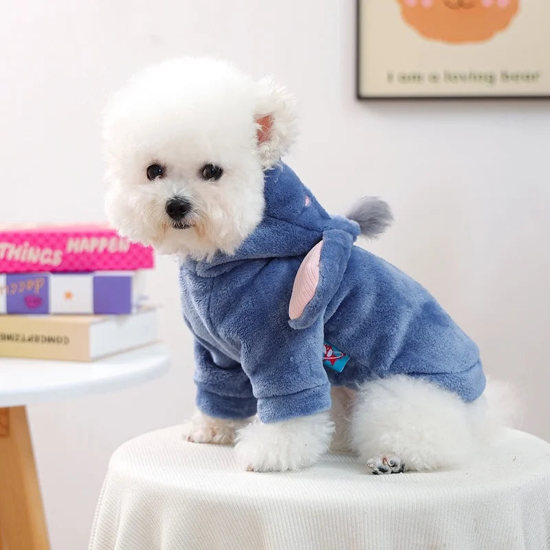 A fluffy white dog wearing a blue seasonal flannel hoodie sitting on a white table.