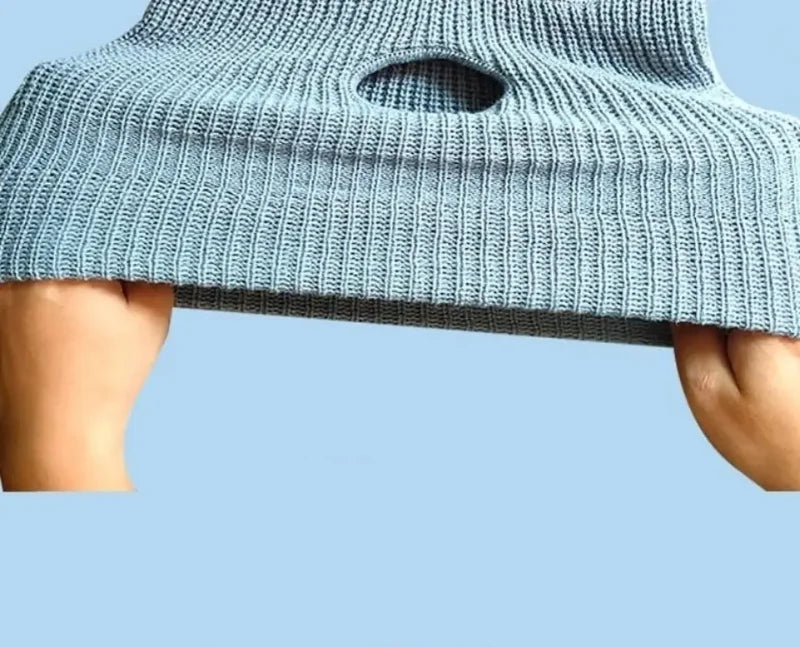 A light blue knitted dog head and warm mask accessory being held by a person's hand.