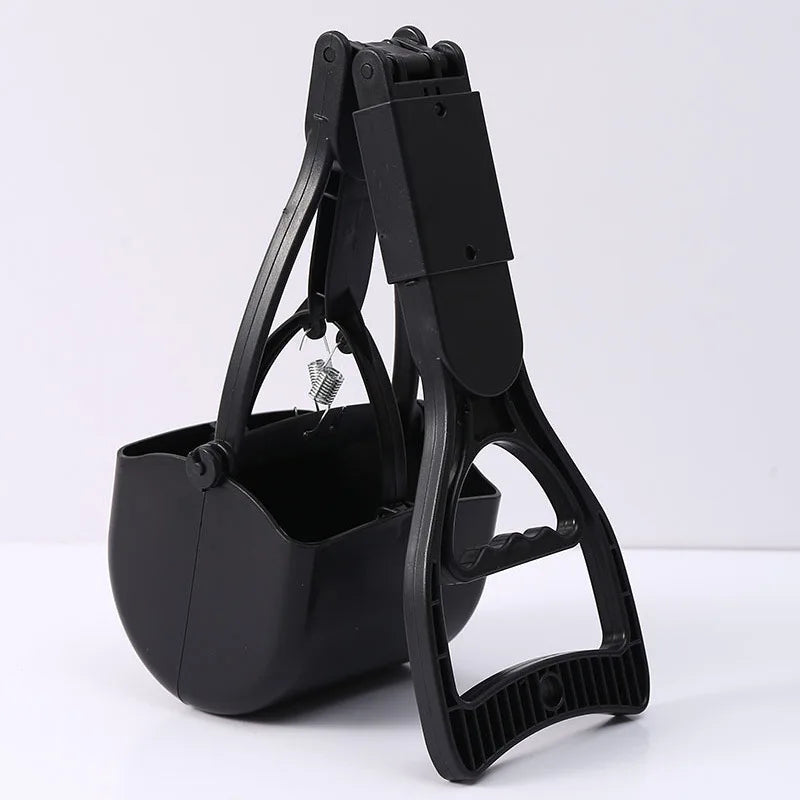 A black portable foldable dog poop scooper with a handle and container is shown on a white surface.