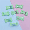 Several bone-shaped hair clips in light green are displayed on a pink and blue background.
