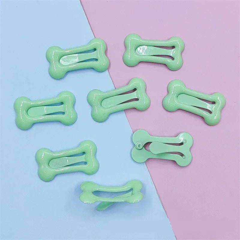 Several bone-shaped hair clips in light green are displayed on a pink and blue background.