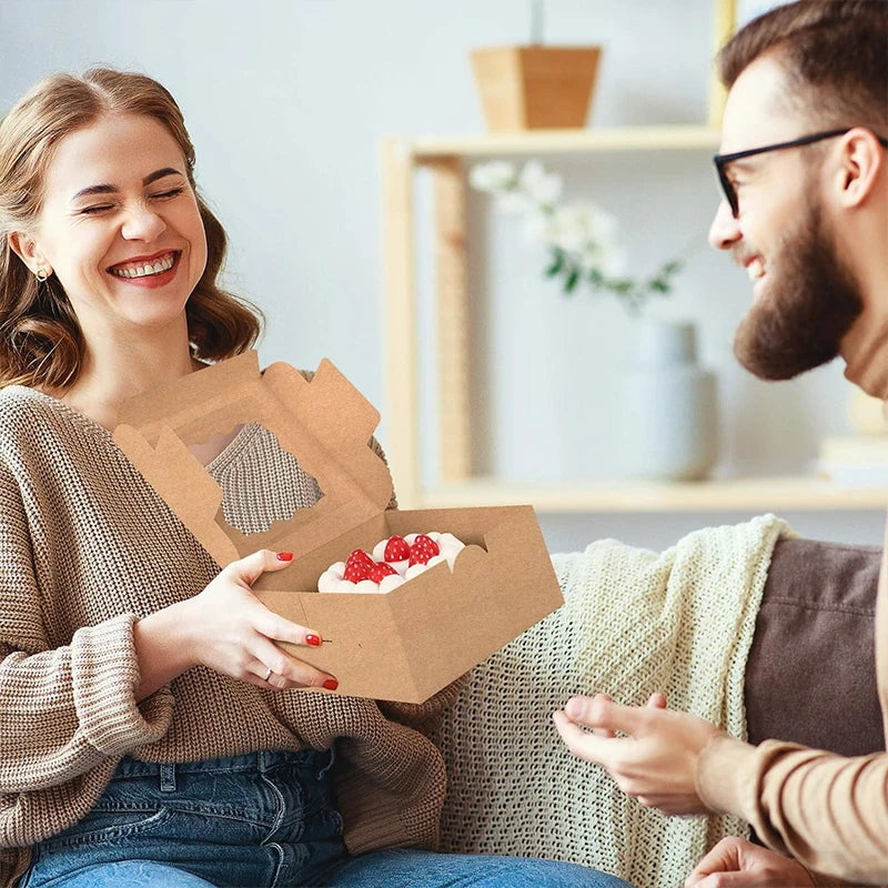A woman is smiling while holding an open cardboard box containing red fruit, suggesting clear window cake boxes.