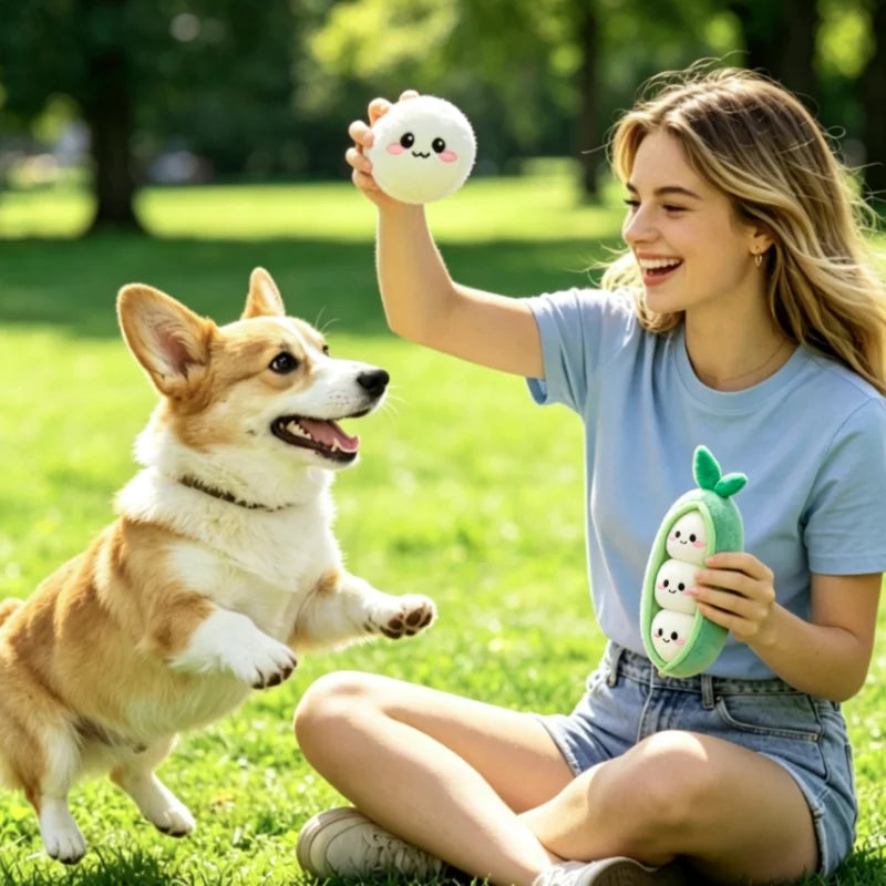 A young woman is smiling while holding a green plush sausage dog chew toy and interacting with a happy dog in a grassy park.