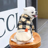 Un perro blanco vistiendo una sudadera con capucha de forro cuadros y detalle de cremallera naranja, sentado sobre una superf
