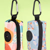 A pair of colorful, zippered poop bag holders with black handles and light blue, pink, and yellow patterned fabric.