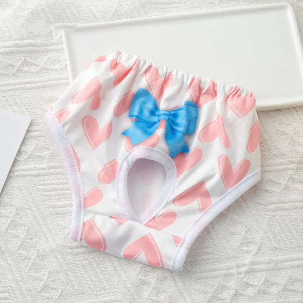 White reusable dog physiological pants with pink hearts and a blue bow displayed on a white tray.