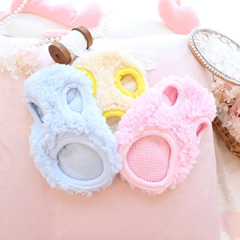 Three fluffy velvet pet sweaters in blue, yellow, and pink resting on a pink fabric.