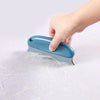 A hand is using a blue portable lint and pet hair remover brush to remove fuzz from a white surface.