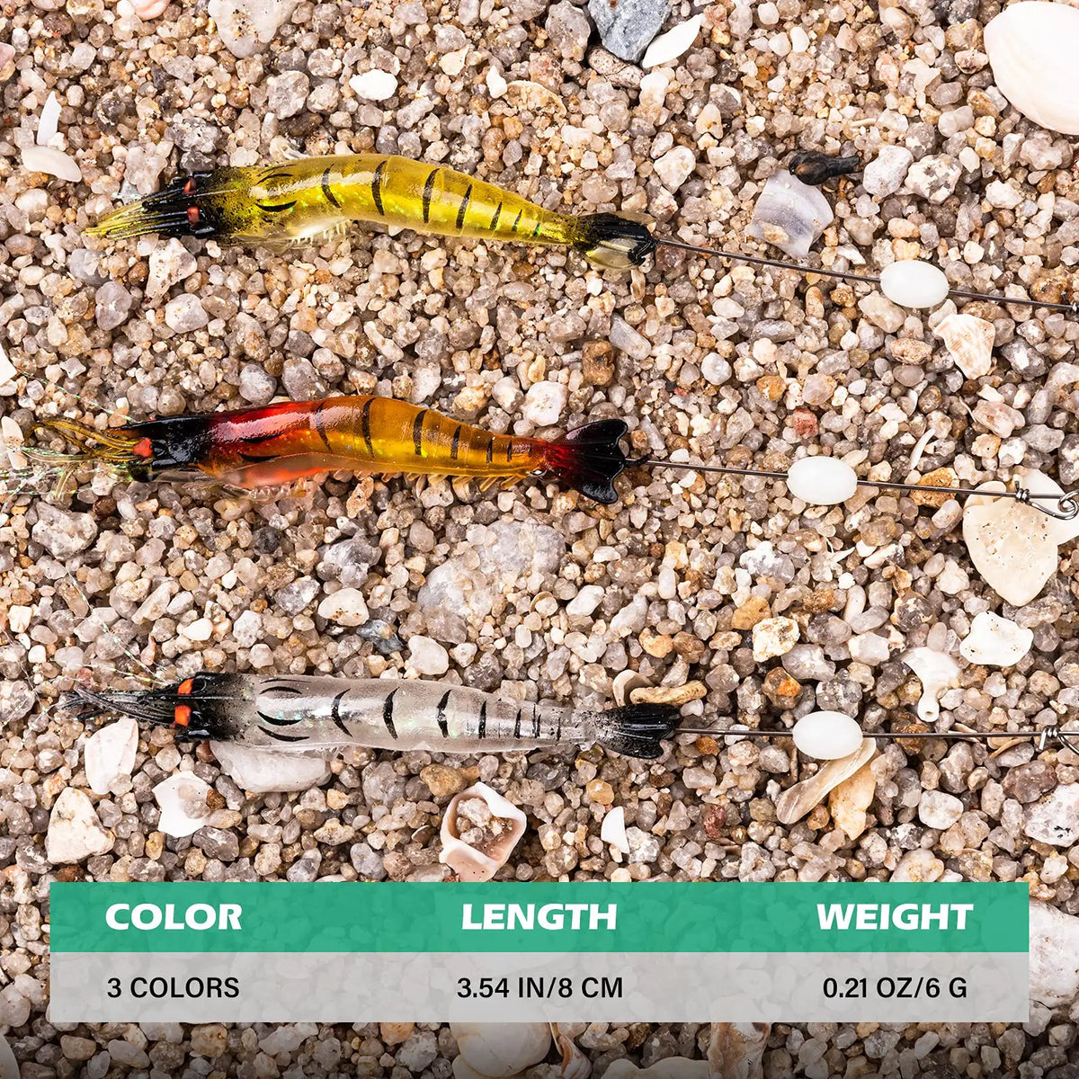 Three luminous soft shrimp lures of varying colors and lengths resting on a gravel surface.