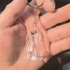 Klares Glasfigur eines Hundewelpen mit goldfarbener Kette und Schlaufe, in der Hand einer Person gehalten.