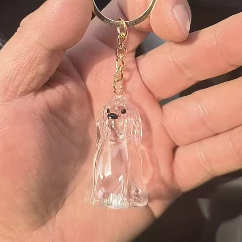 Klares Glasfigur eines Hundewelpen mit goldfarbener Kette und Schlaufe, in der Hand einer Person gehalten.