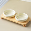 Two white ceramic bowls for pets are displayed on a wooden stand.