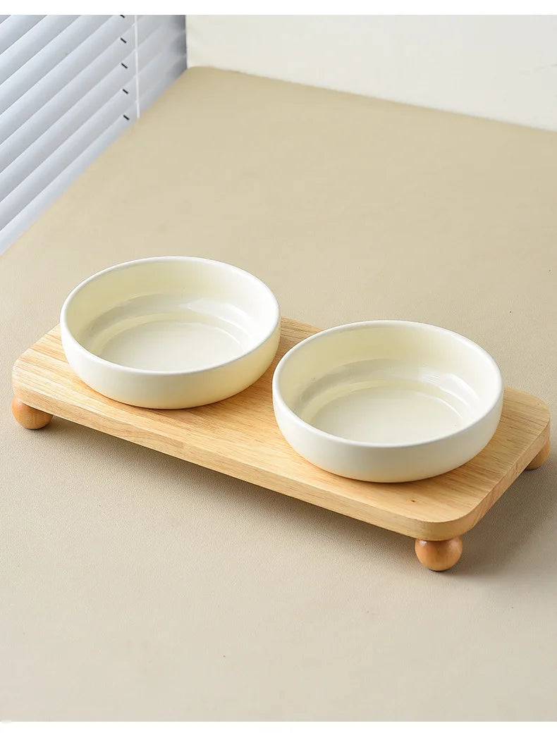 Two white ceramic bowls for pets are displayed on a wooden stand.