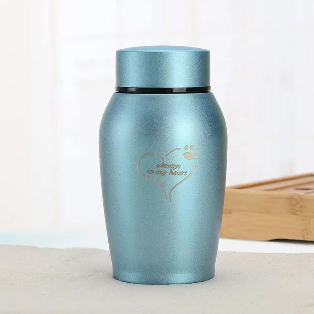A light blue stainless steel pet memorial storage box with a heart and paw print engraved on the side.