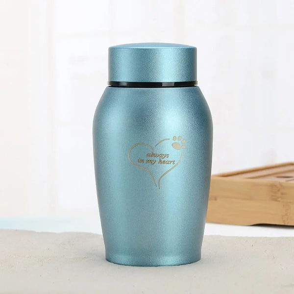 A light blue stainless steel pet memorial storage box with a heart and paw print engraved on the side.