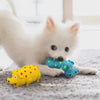 A white dog lies next to a bright yellow squeaky toy pig and a blue squeaky toy dinosaur on a gray surface.