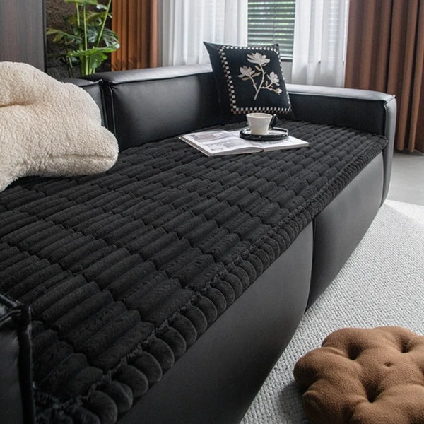 A black plaid flannel pet seat protector and car mat placed on a dark leather sofa.
