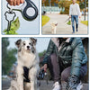A person is using a hands-free dog poop bag dispenser with a leash clip to pick up dog waste.