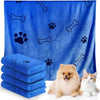 A bright blue ultra-soft quick-dry pet bath towel featuring paw print and bone patterns, with stacked towels and a small dog 