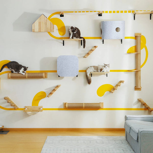 A white wall features a wooden and sisal cat scratching post rack with various sized posts and a gray cat sitting on one.
