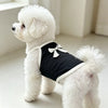 A fluffy white dog wearing a black ribbed vest with a white bow knot.