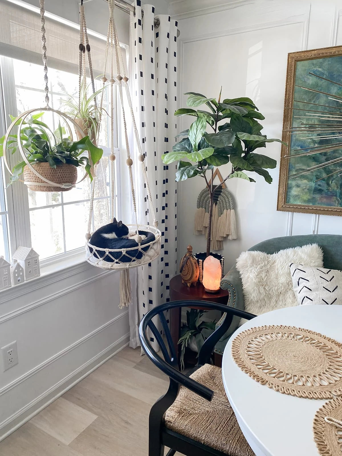 A bohemian macrame cat hammock bed for pet decor hangs by a window, decorated with plants and natural fibers.