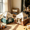 A beige and brown breathable mesh foldable pet tent is displayed on a wooden floor near a window.