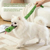 A white fluffy dog is playing with a green crinkle snake toy, showing an interactive bond between the owner and pet.