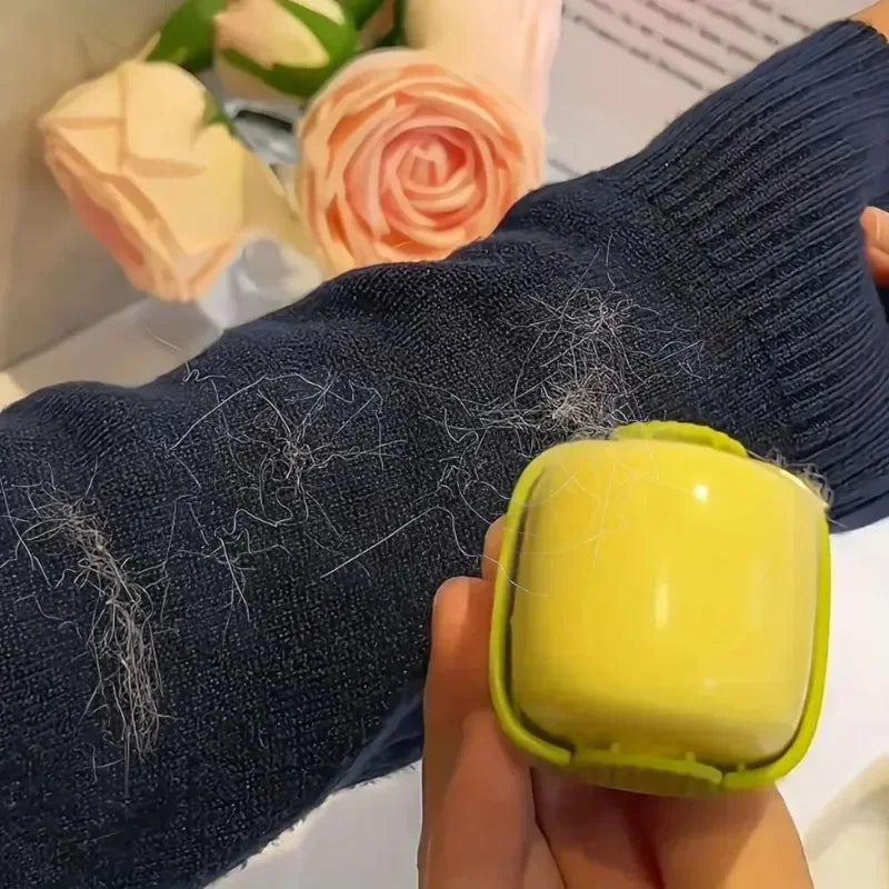 A hand holds a yellow portable lint roller against a dark blue knitted sleeve.