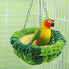 A yellow and green parrot is perched inside a green moss hanging hammock in an aviary.
