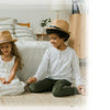 A young boy and girl sitting on a light-colored rug with a cat next to them in a bright bedroom.
