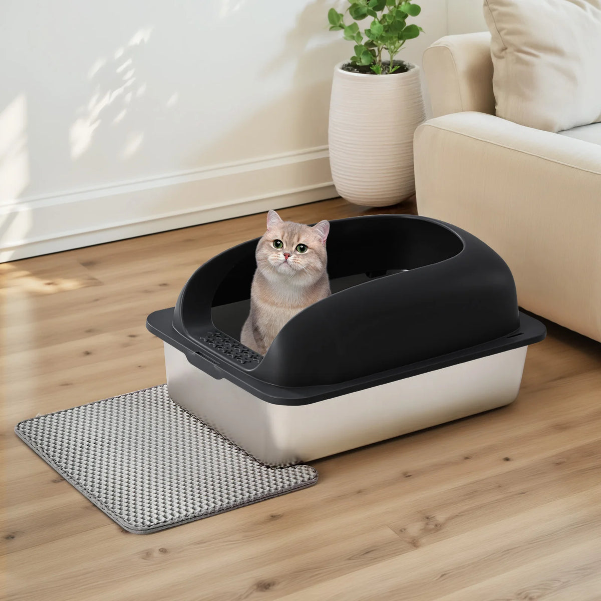 Une grande litière pour chat en acier inoxydable avec pelle et tapis, posée sur un plancher en bois.