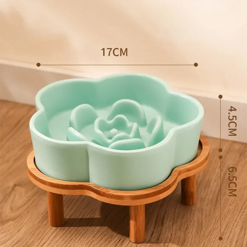 A light mint green ceramic slow feeder cat bowl rests on a natural wooden stand.