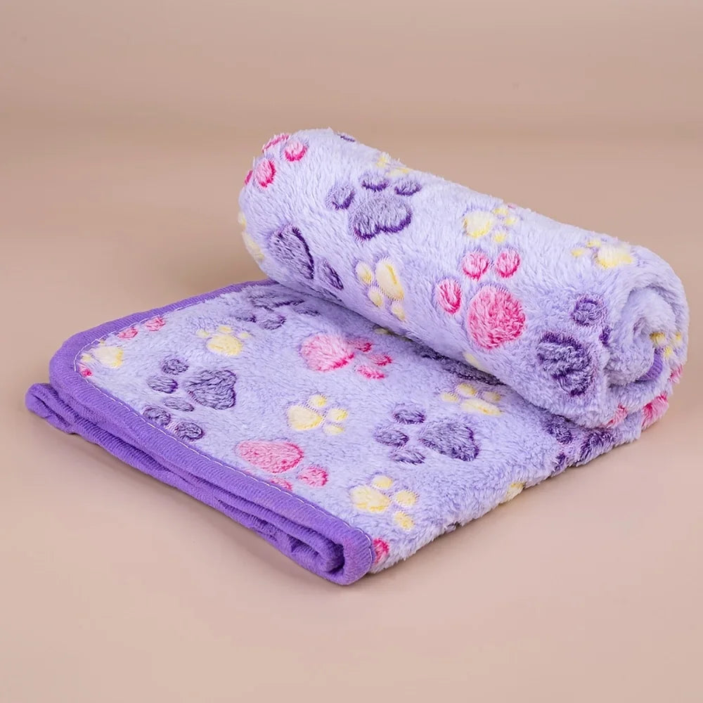 A rolled soft pet fleece blanket in purple with pink and yellow paw print designs.