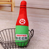 A red and green bottle-shaped plush dog toy with a paw print design is placed in a wire basket.