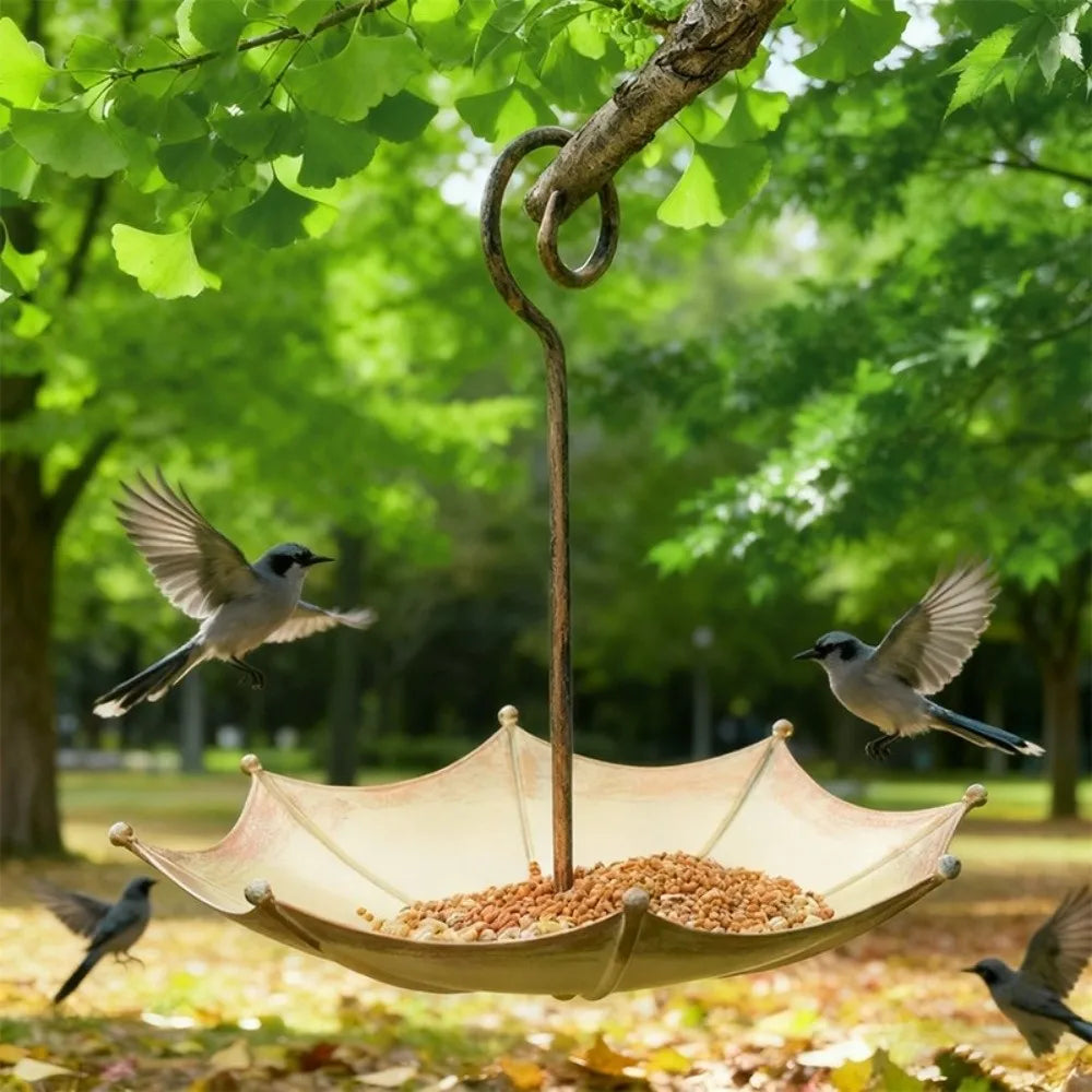 An umbrella-shaped hanging bird feeder with a wooden pole and a wide, light-colored dish is suspended from a tree branch.