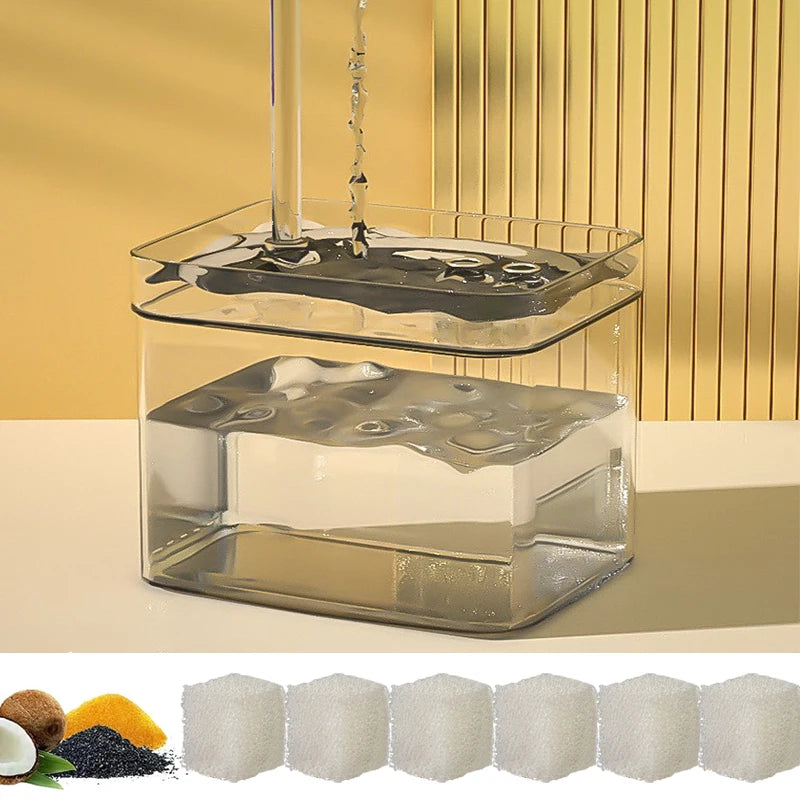 A clear glass water fountain with an activated carbon replacement filter assembly and several blocks of white activated carbo