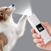 A hand holds a white pet nail grinder device, which is emitting a bright light onto a dog's paw.