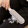 A hand is using a white lint remover brush with a gray head to remove pet hair from black fabric.