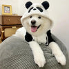 A white dog wearing a black and white panda-themed fleece hooded coat is sitting on a gray textured surface.