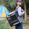 A woman is carrying a gray ventilated bird travel backpack with a perch and feeding cups outdoors.