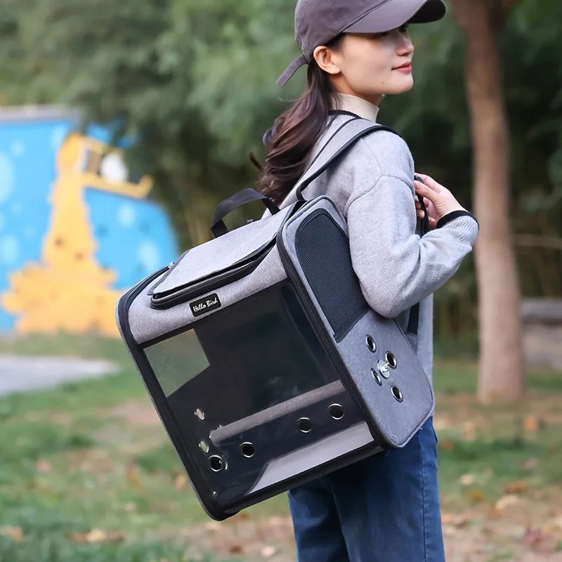 A woman is carrying a gray ventilated bird travel backpack with a perch and feeding cups outdoors.