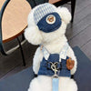 A fluffy white cartoon dog plush wearing a blue and white plaid harness vest with a leather tag and chain.