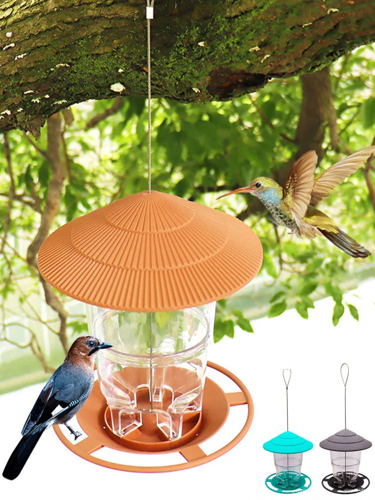 Orange wasserdichtes Vogelfutterspender, aufgehängt an einem Ast, mit Glasschale und kleinen türkisen Futtererger.