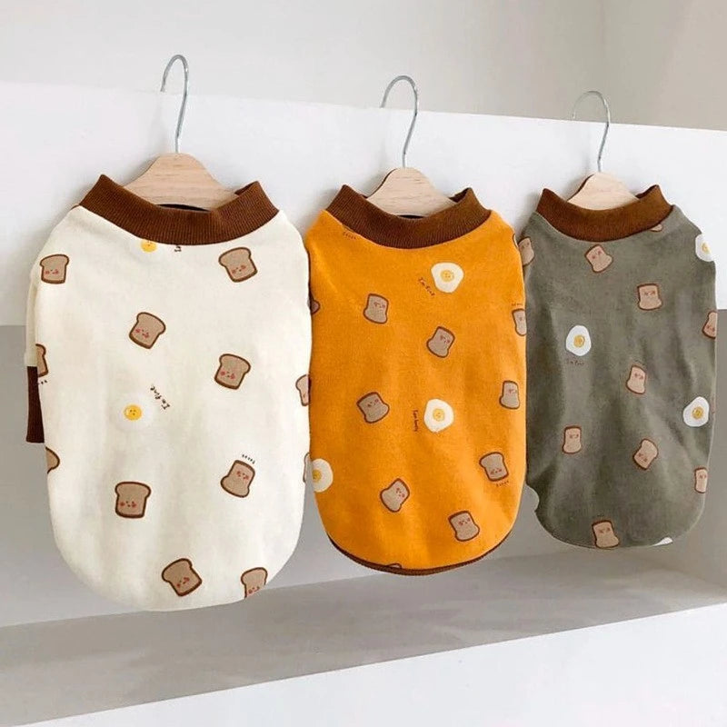 A beige cartoon print dog vest hanging on a wooden hanger.