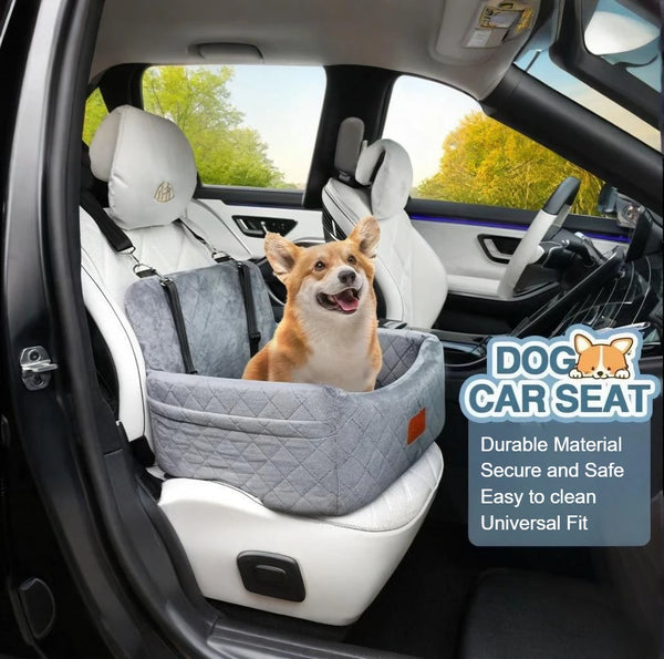 A small dog is sitting in a gray pet car seat inside a car, next to the driver's seat.