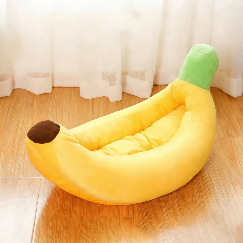 A yellow banana-shaped plush pet bed with a green tip resting on a wooden floor.