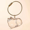 Un charm en verre clair en forme de chat attaché à un anneau de clé en or tressé.