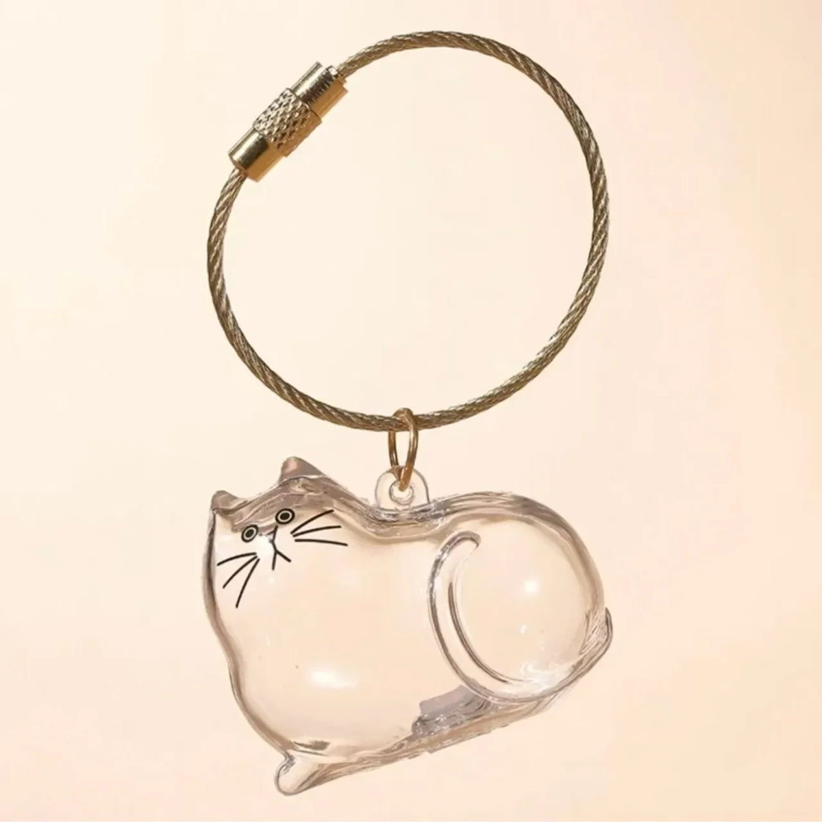 Un charm en verre clair en forme de chat attaché à un anneau de clé en or tressé.
